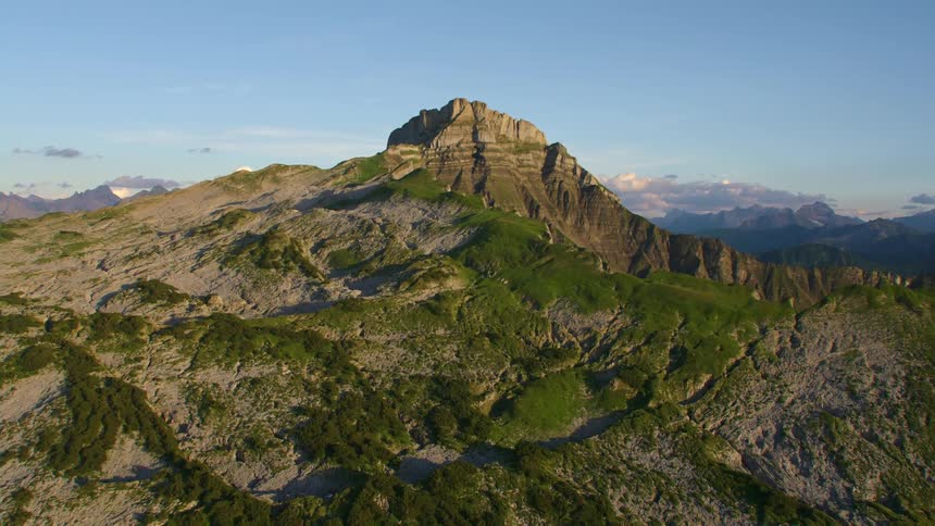 Summit of extended vegetation covered mountain stands under cloudy sky