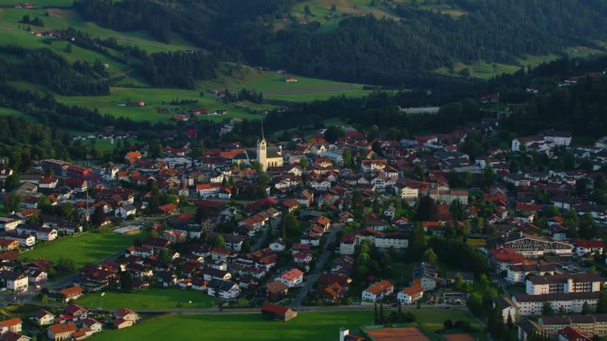 A church is surrounded by many buildings in a in a valley community and there are mountains in the distance