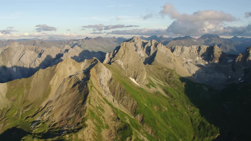 Portions of vegetation covered craggy mountains remain in light and parts remain in shadow