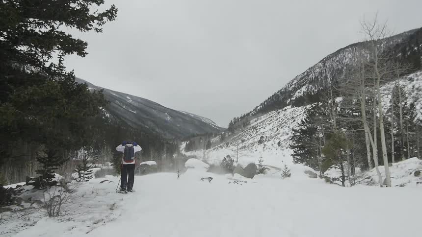 A hiker is stopped adjusting their cap on a wind-blown snowy hillside