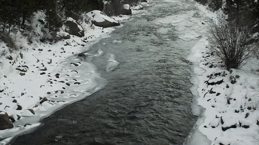 A stream runs through a hilly valley covered with snow