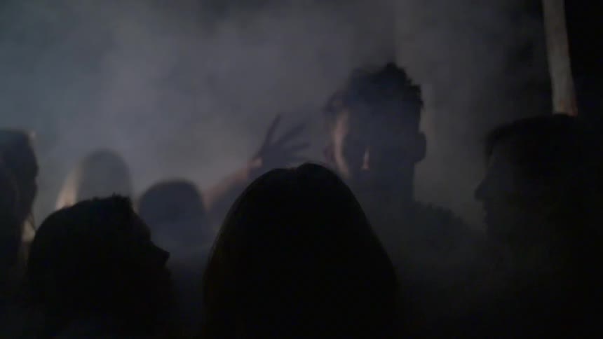 A man walking through a crowd of women as they reach out to touch him in a smoky room