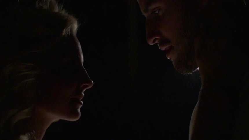 A man and woman stand close as she touches him