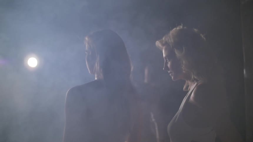 A woman walking through a group of other women in a smoky room