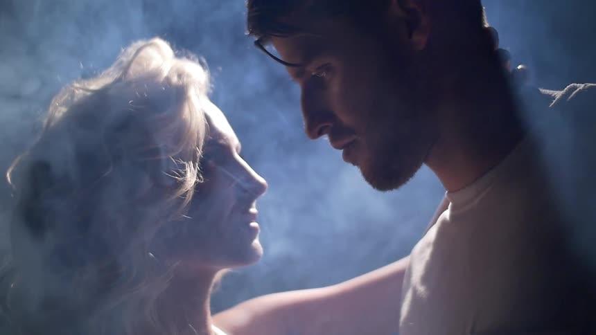 A woman is holding a man close in a smokey area