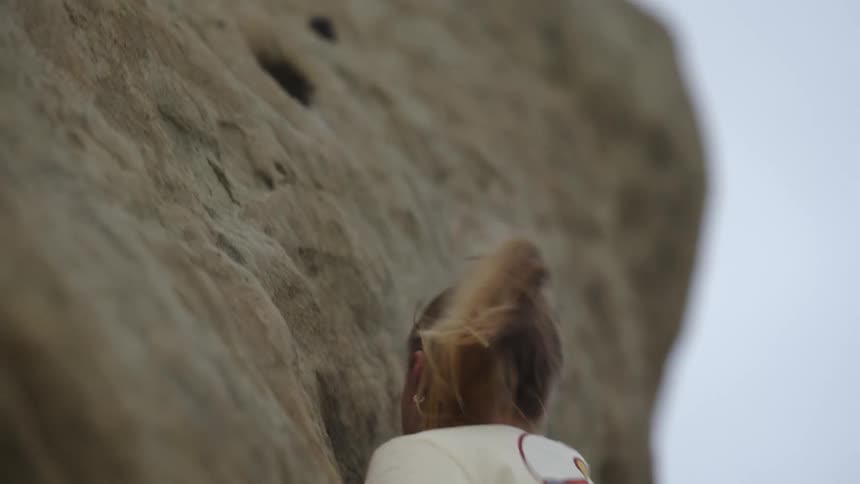 Woman climbs up cliff outdoors on a windy day