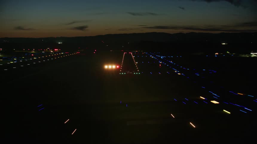 Airplane Landing at night time lapse on a runway lit up at night with traffic and cars zooming by in the background with blue sunset light still in the sky