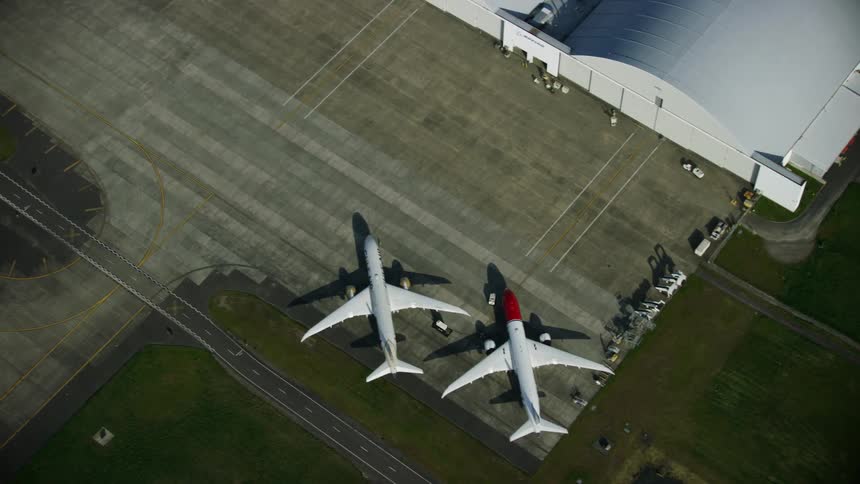 Looking straight down on two Boeing 787-9 dreamliner aircraft at a large hangar as the camera flies high above the airport in this aerial shot
