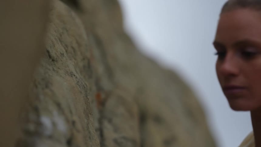 A woman is holding on to rocks as she climbs up the side of a mountain