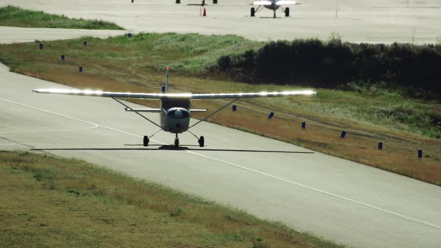 Sun glistens off the wings of a small Cessna single engine aircraft as it taxis down the runway towards take off at a small airfield