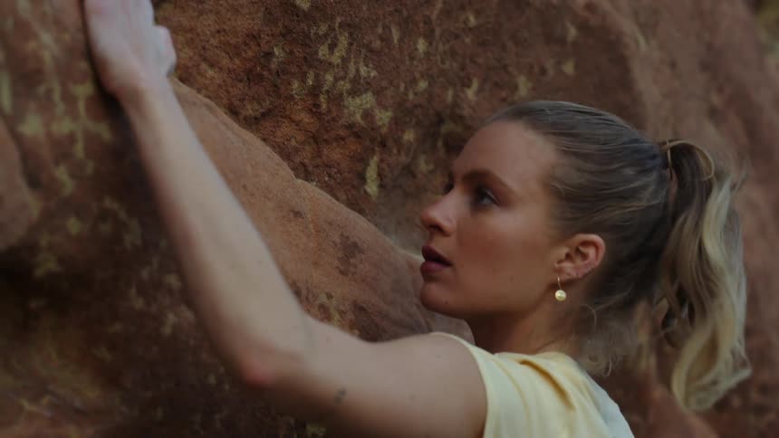 Young blonde woman pushes herself up while climbing a rock wall
