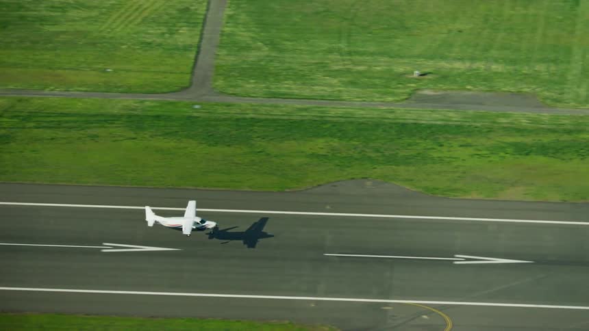 A Cessna Caravan touches down at a large airport as seen by a shadow first and then the landing Cessna single engine airplane next