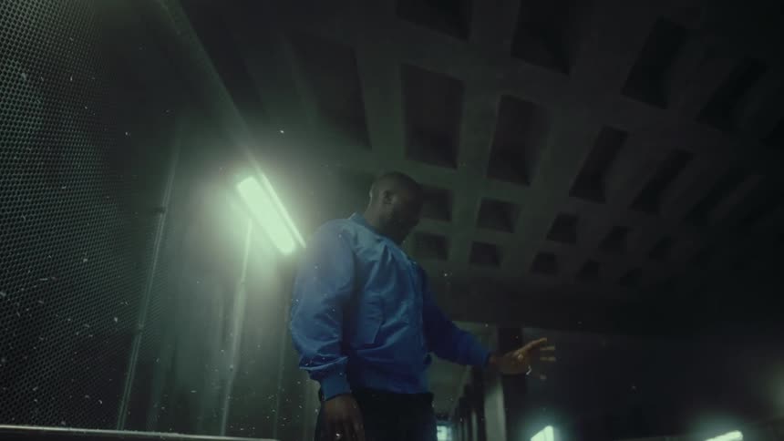 White confetti falls over a young man standing inside a tunnel with his hand raised to the ceiling