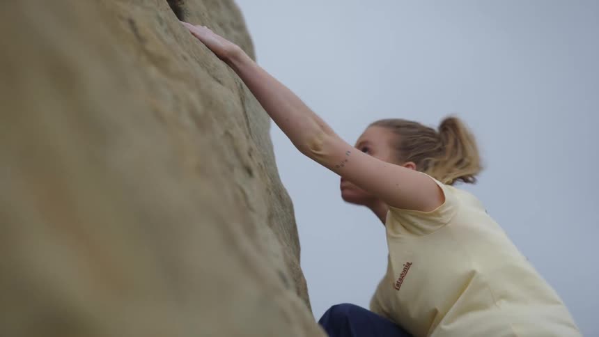 Young blonde woman pushes herself up while climbing a rock wall on a mountain