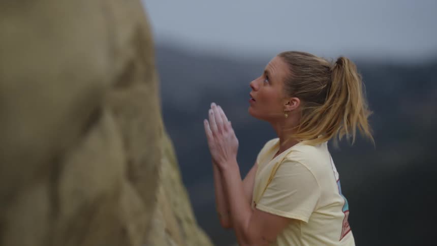 Woman about to climb rock wall rubs chalk on to her hands