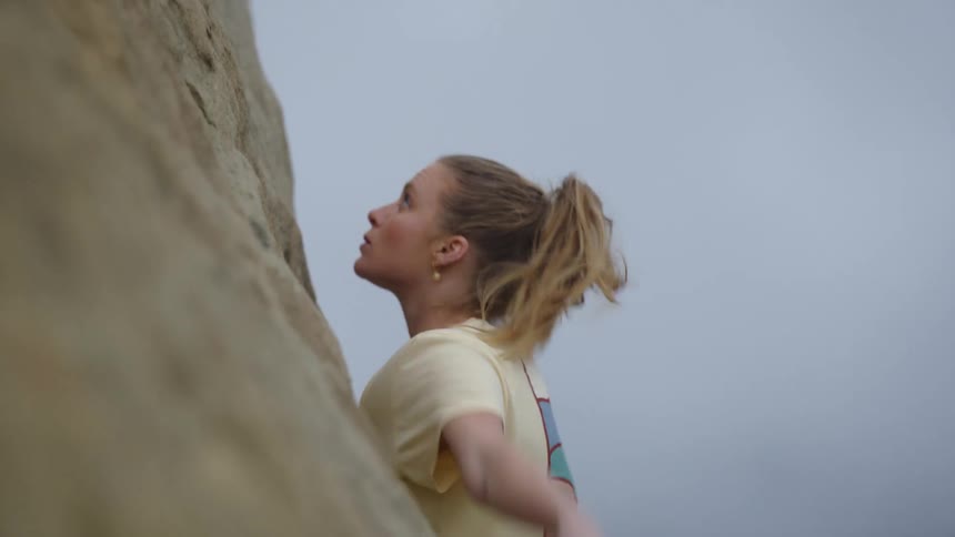 A woman free climbing reaches up to grasp a handhold on a rock