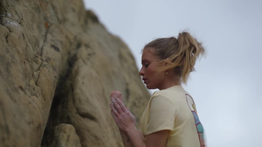 A rock climber rubs chalk onto her hands and prepares to climb up