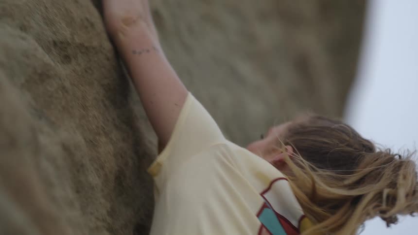 A young woman rock climbing outside on a breezy day