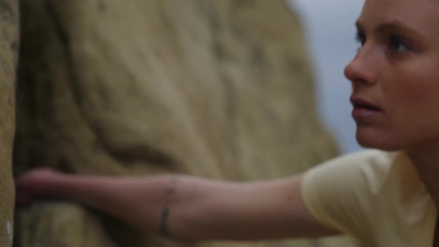 A woman climbing up the side of a mountain looks around for her next move