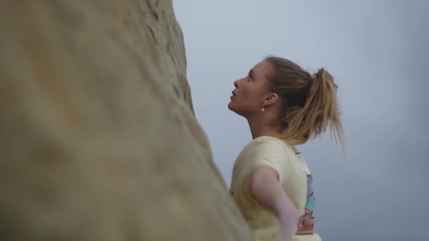 Blonde woman with her hail in a pony tail climbs up the rocks on a breezy day
