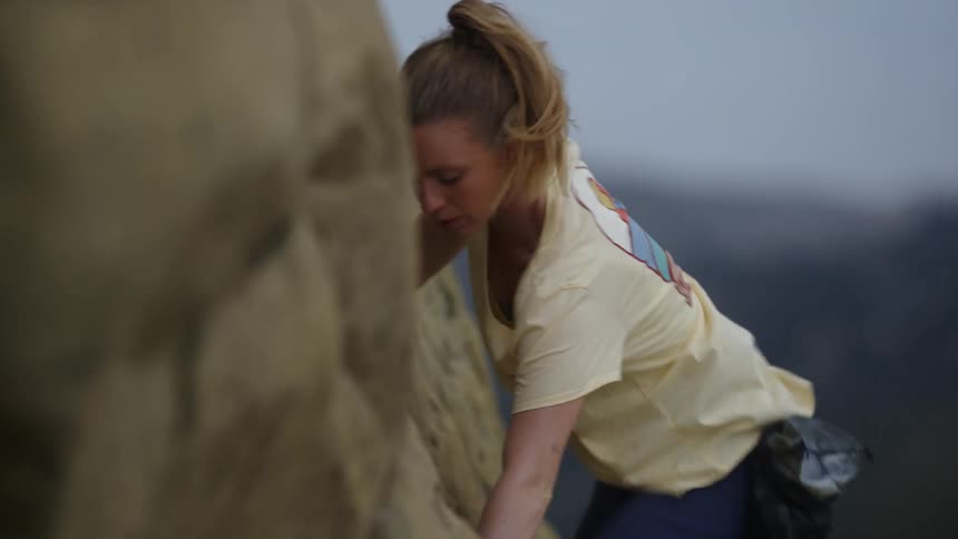 Young blonde woman pushes herself up while climbing a rock wall