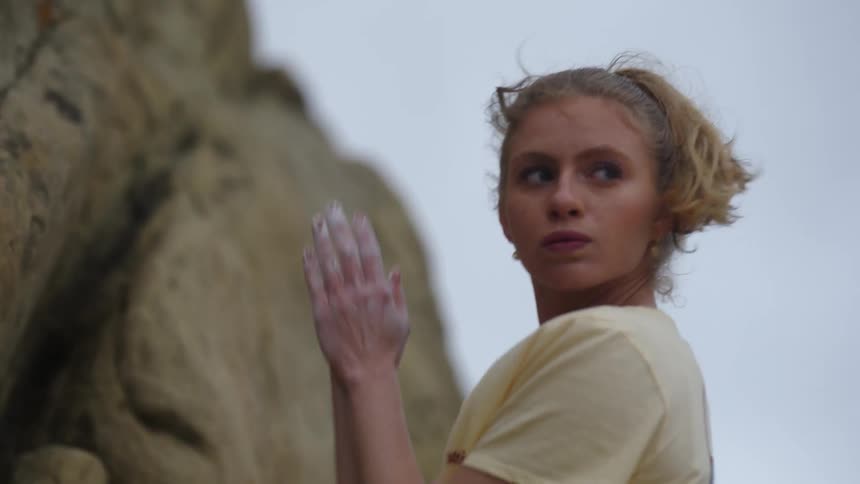 Young woman with limb difference rubs her hand with white talcum before climbing a rock wall