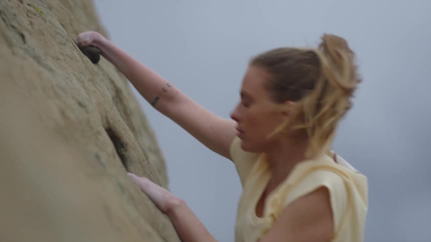 A determined woman skillfully climbs up a steep cliff while rock climbing