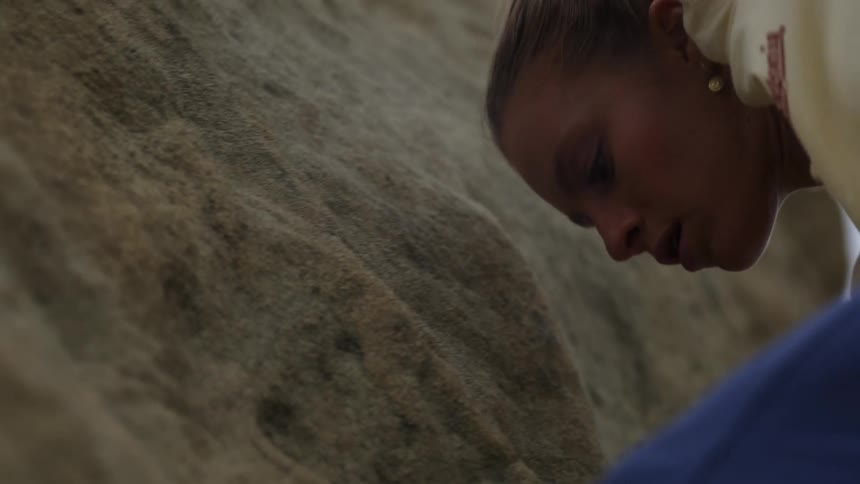 A rock climber looks back and down to check her foothold as she pulls herself up