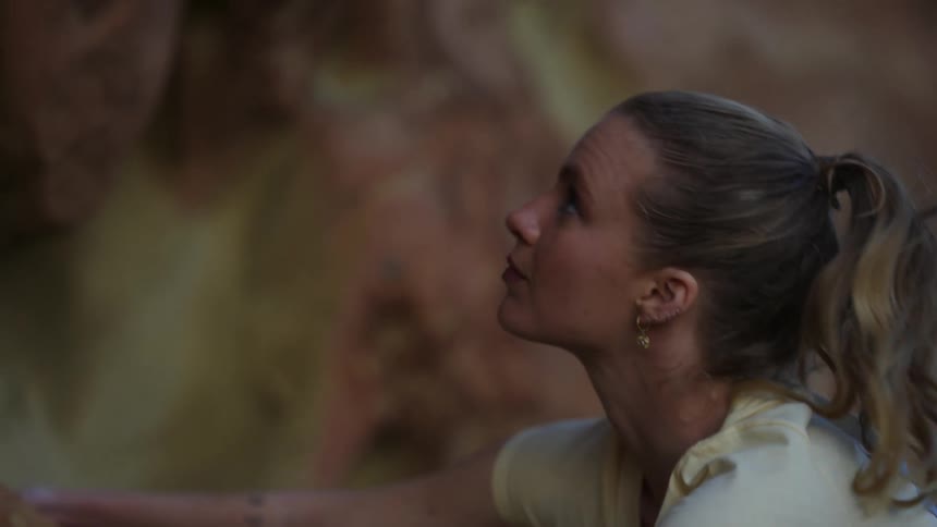 A woman looks up at the rock above her while climbing a natural rock face outdoors during the day