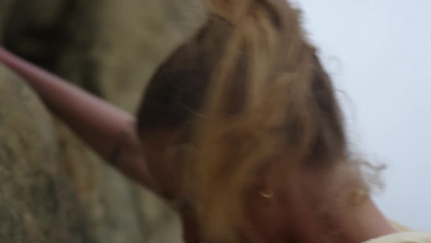 A woman reaches up and climbs up a sheer rock face