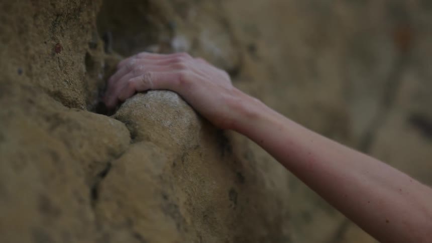 A rock climber gripping the side of a cliff with their hand