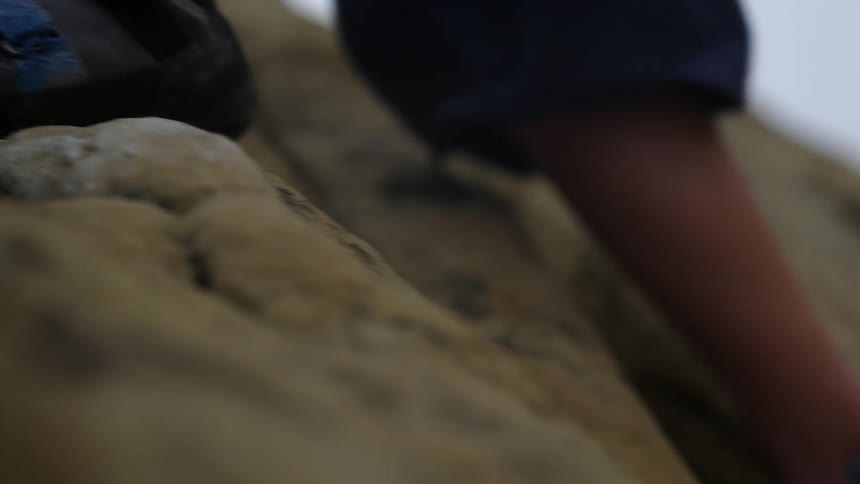 Rock climber in blue pants and wearing blue footwear climbs up the rocks