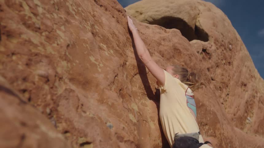 A woman climbing up a sheer rock face reaches up above her head for a handhold