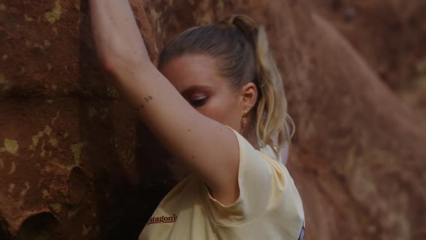 A woman is climbing the side of a mountain and looks up as she is holding on to rocks