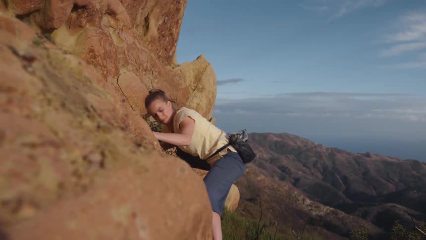 Young blonde woman pushes herself up while climbing a rock wall on a mountain