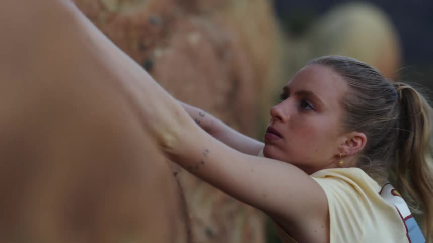 A woman is reaching for rocks to hold on to as she climbs the side of a mountain