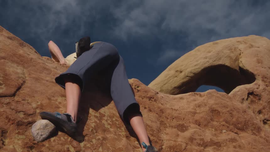 A female rock climber making it to the top of a rocky cliff