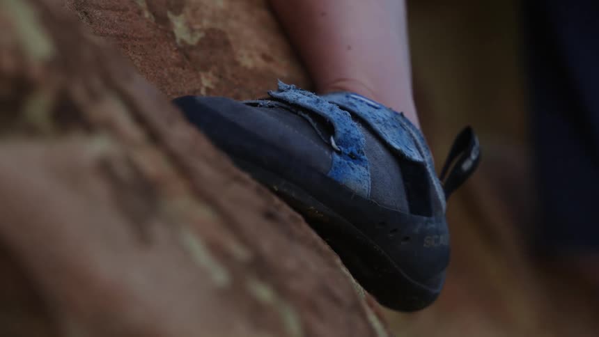 Climber maneuvers their feet up rock wall while climbing