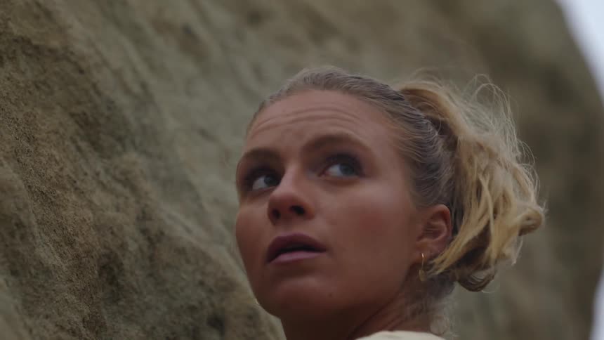 A woman who is rock climbing pauses to look off into the distance
