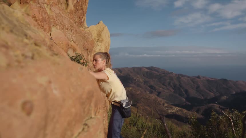 A woman hoists herself up the edge of a mountain as she rock climbs