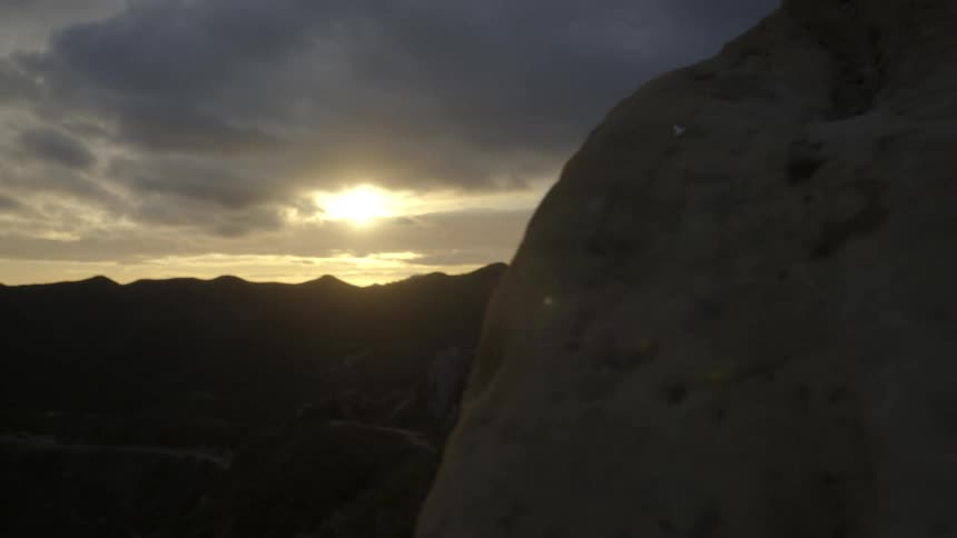 The sun peaks through thick clouds over a stone mountain ridge