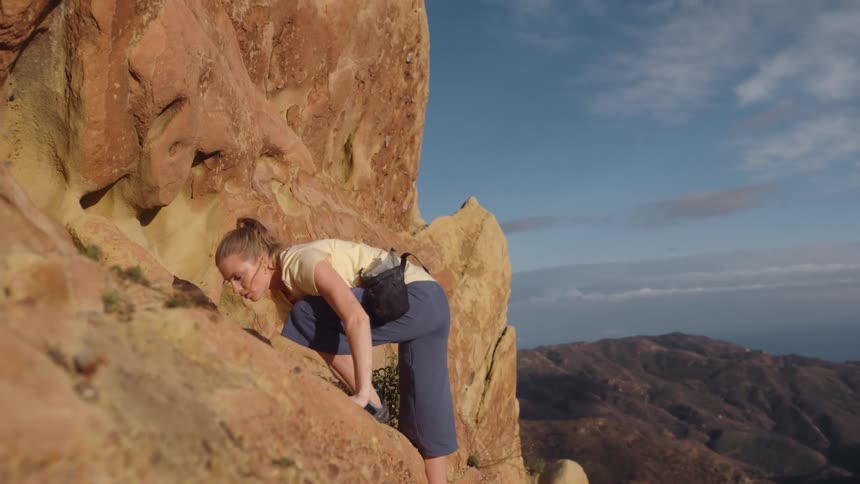 A woman climbs onto a ledge on the side of a mountain