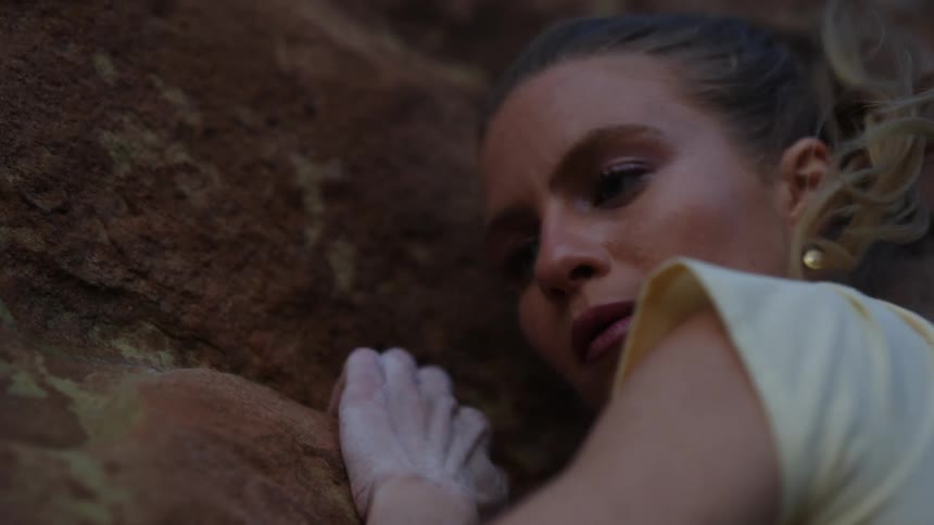Young blonde woman pushes herself sideways while climbing a rock wall