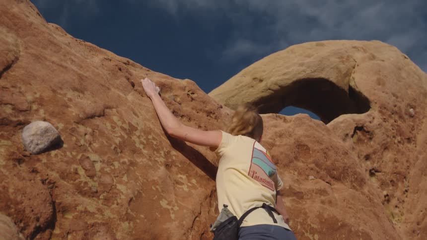 A woman holds onto a rock ledge pulling herself up as she climbs