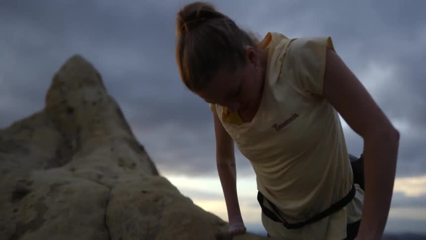 A woman uses her strength to pull herself to the top of a cliff while rock climbing