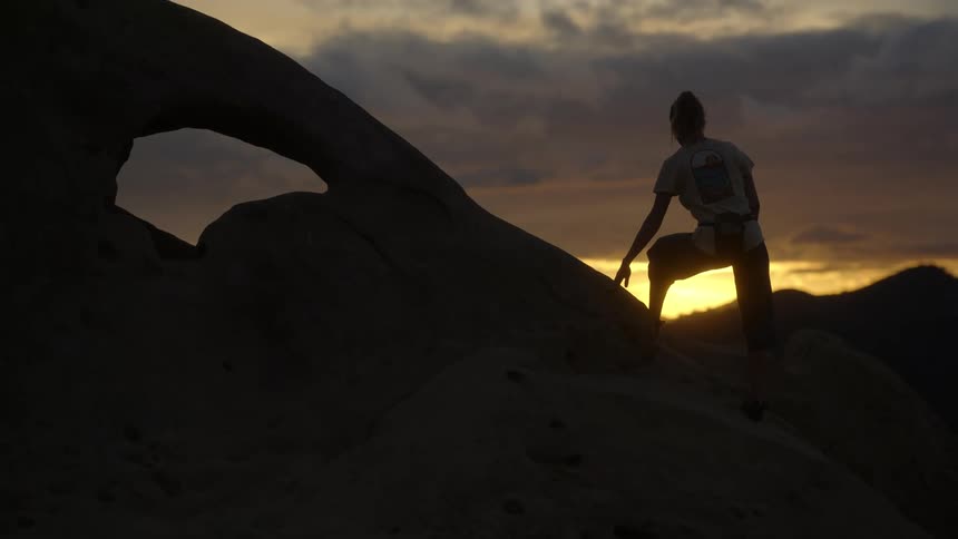 A woman climbing on large rocks in the wilderness at sunset