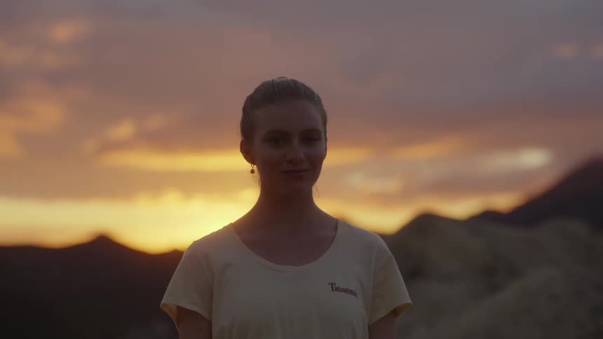 Blonde woman stands and smiles as mountains sit behind her at dusk