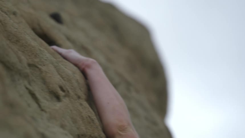 A woman reaches for a hole to grip while rock climbing