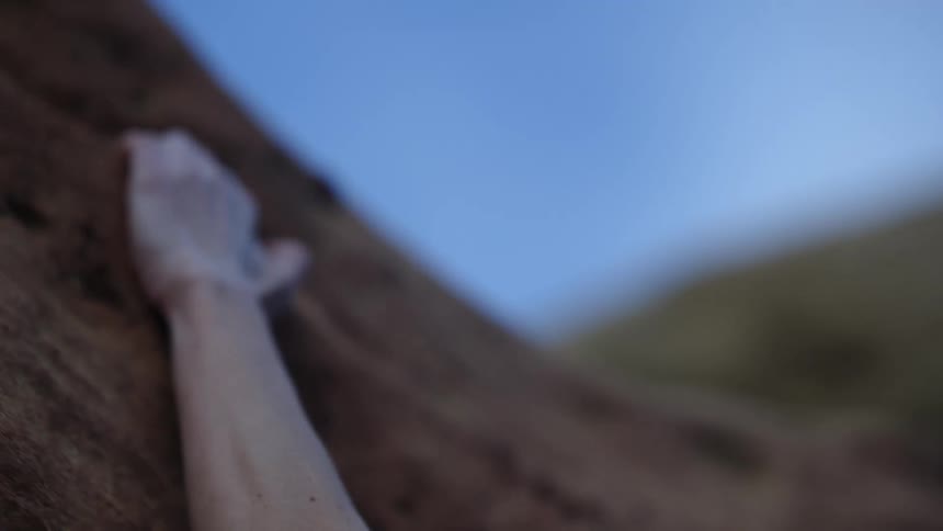 A woman climbing a rock reaches up above her head with one hand