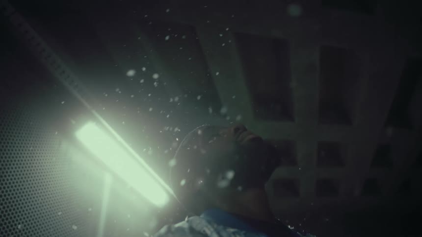 A man is standing in a room with a bright light and looking up as small white objects float down in the air like snow